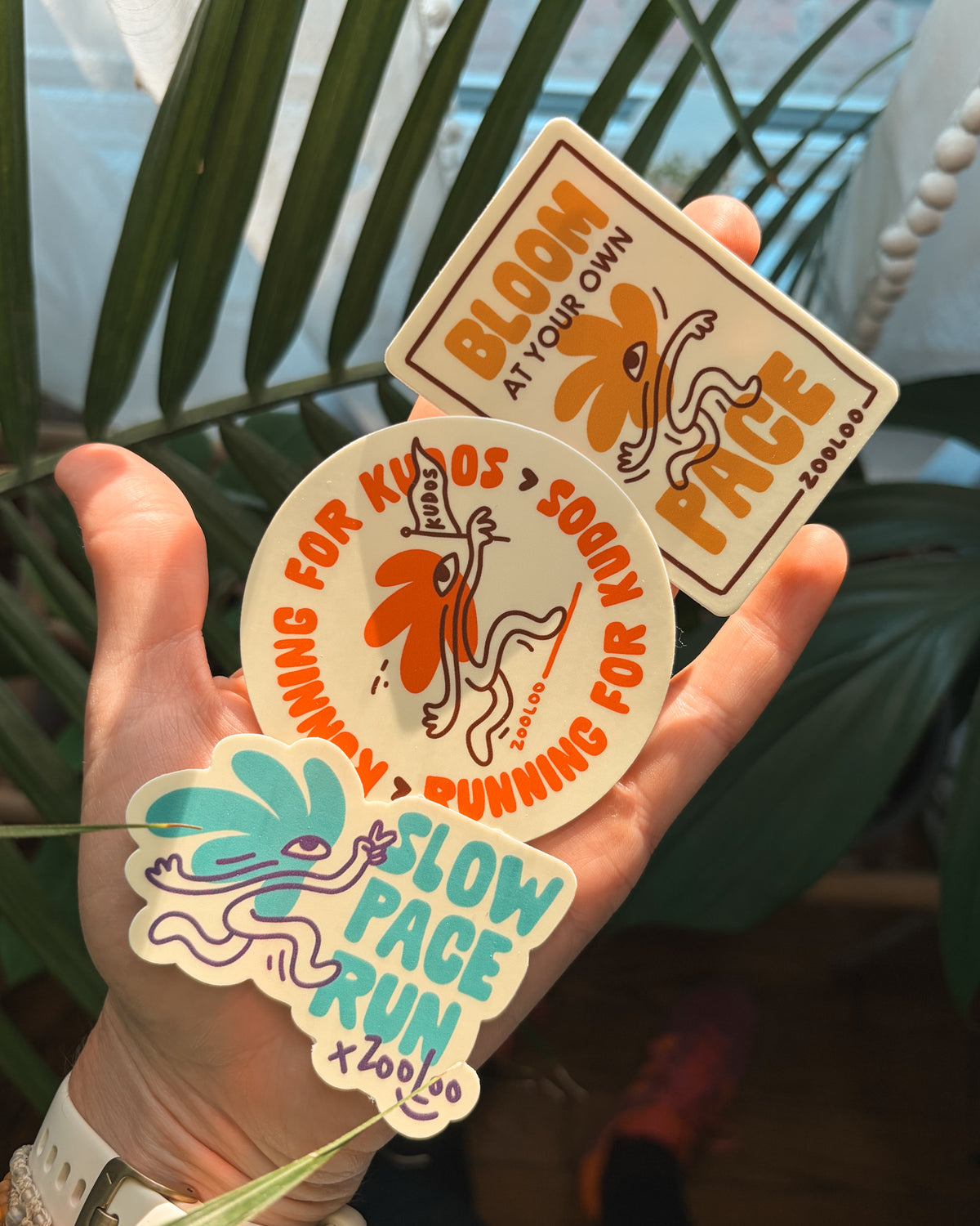 Slow Pace Run Club sticker collection by Zooloodesign: Slow Pace Run, Running For Kudos and Bloom At Your Own Pace running stickers held in hand