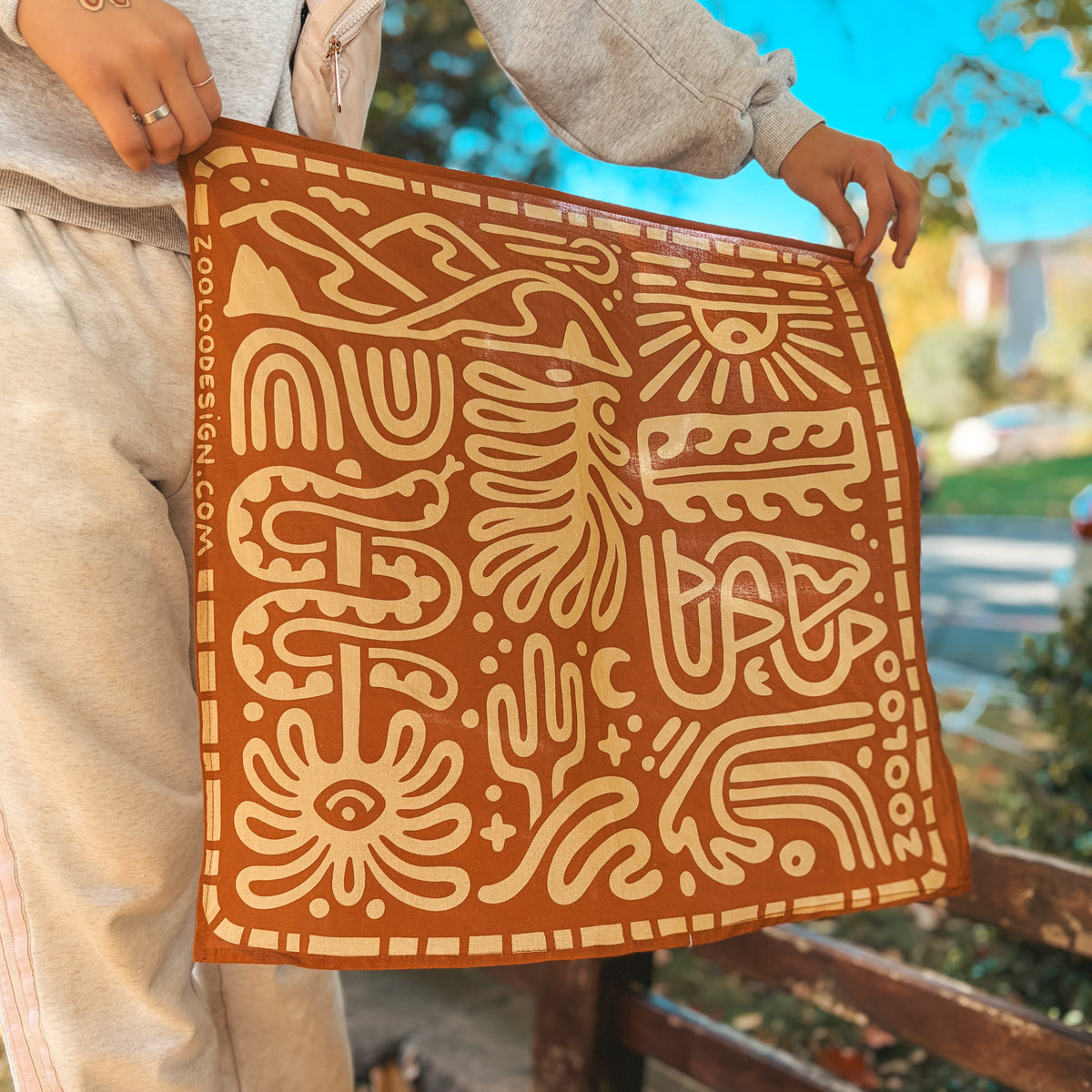 Rust Zooloo Design boho bandana with cream desert and surf print, held outdoors